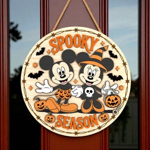 May include: A round wooden Halloween door sign featuring Mickey and Minnie Mouse in Halloween costumes. The sign reads "Spooky Season" in orange letters and includes bats, pumpkins, and stars.