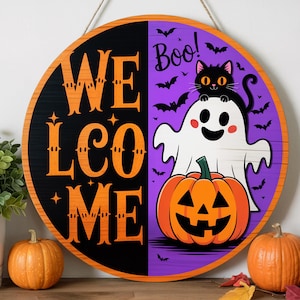 Puede incluir: Cartel de bienvenida de Halloween de madera redonda con un diseño negro y naranja. El cartel presenta la palabra "WELCOME" en naranja, un fantasma, un gato negro, una calabaza y la palabra "Boo!" en blanco.