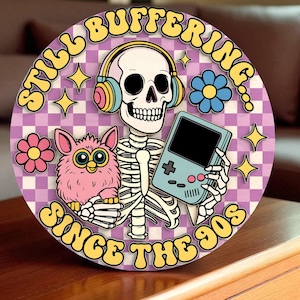 May include: Round graphic with a skeleton wearing headphones and holding a handheld game console, with a pink Furby. The background is a purple and white checkerboard pattern. Text reads "Still Buffering Since the 90s."
