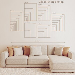May include: An art print size guide with various aspect ratios and dimensions is displayed on a wall. A beige sofa with throw pillows sits below the guide. The text "ART PRINT SIZE GUIDE" is visible.