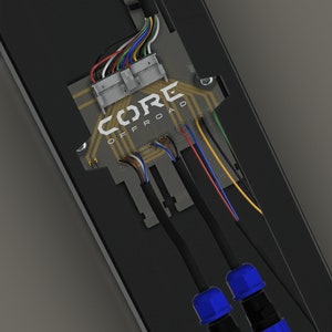 May include: A close-up of a black electrical panel with a circuit board labeled "CORE OFFROAD". The panel has multiple wires connected to it, including two blue connectors.