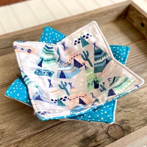 May include: A teal and white fabric bowl with a geometric pattern of tents and cacti. The bowl is folded and sitting on a wooden surface.