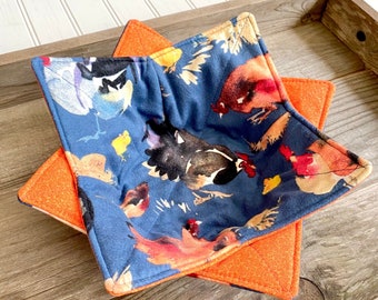 May include: A set of two blue and orange pot holders featuring a pattern of chickens and roosters. The pot holders are made of fabric and have a quilted texture.