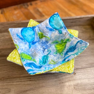 May include: A blue and green fabric bowl with a sea turtle pattern. The bowl is folded into a star shape.