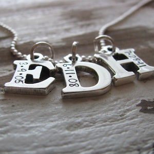 Peut inclure: Collier en argent avec trois breloques, chacune une lettre avec une date grav&eacute;e dessus. Les lettres sont E, D et H. Les dates sont 3-9-05, 8-11-06 et 11-22-87.