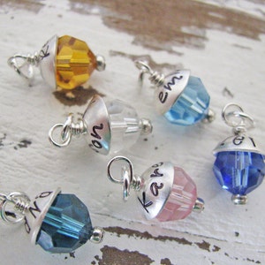 Peut inclure: Six pendentifs en argent avec des perles de cristal. Chaque pendentif a une perle de cristal de couleur différente et une inscription personnalisée. Les inscriptions comprennent "Ray", "Em", "No", "Kay", "Zo" et "Lo".