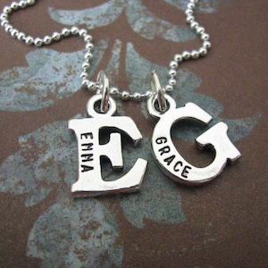 Peut inclure: Un collier en argent avec deux pendentifs, l'un avec la lettre "E" et le mot "Emma" grav&eacute; dessus, et l'autre avec la lettre "G" et le mot "Grace" grav&eacute; dessus.