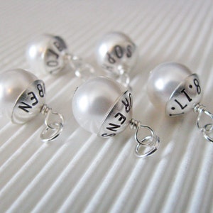 Peut inclure: Cinq perles blanches avec des breloques en argent. Chaque breloque porte un mot différent gravé : "LOVE", "HOPE", "BEEN", "ORENS" et "LIT:8".