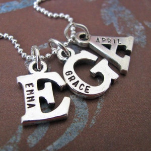 Peut inclure: Collier en argent avec quatre breloques, chacune une lettre avec un nom inscrit dessus. Les breloques &eacute;pellent "Emma, Grace, April".