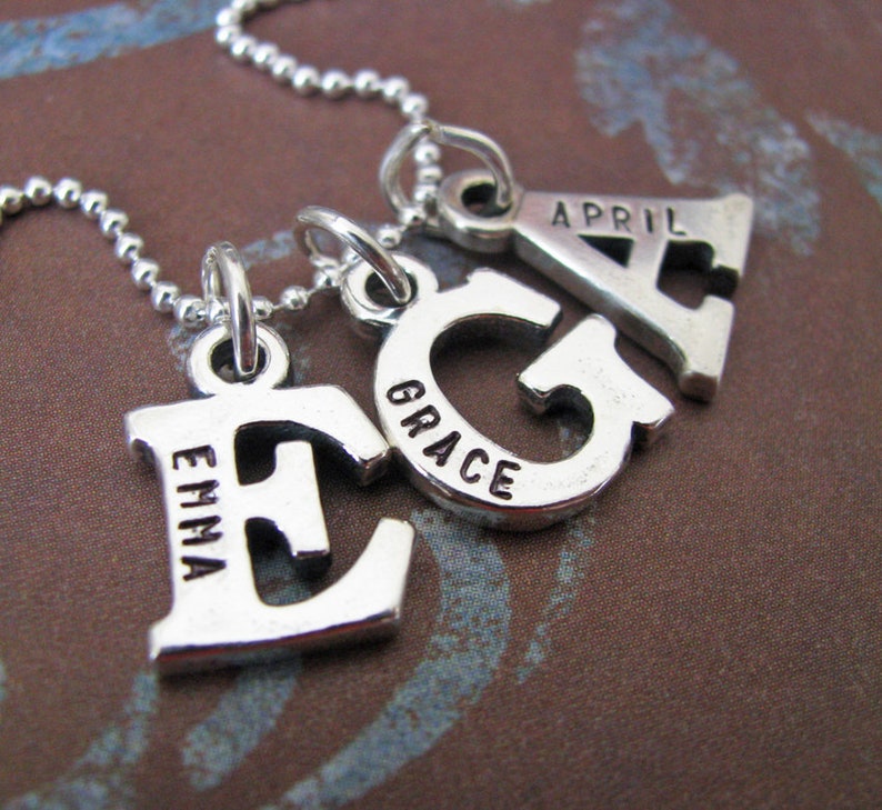 Peut inclure: Collier en argent avec quatre breloques, chacune une lettre avec un nom inscrit dessus. Les breloques &eacute;pellent "Emma, Grace, April".