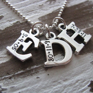 Peut inclure: Collier en argent avec trois pendentifs&nbsp;: une lettre E avec la date 05.06.93, une lettre D avec la date 08.11.80 et une lettre H avec la date 7.28.11.