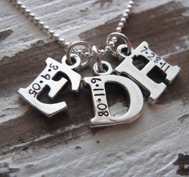 Peut inclure: Collier en argent avec trois pendentifs&nbsp;: une lettre E avec la date 05.06.93, une lettre D avec la date 08.11.80 et une lettre H avec la date 7.28.11.