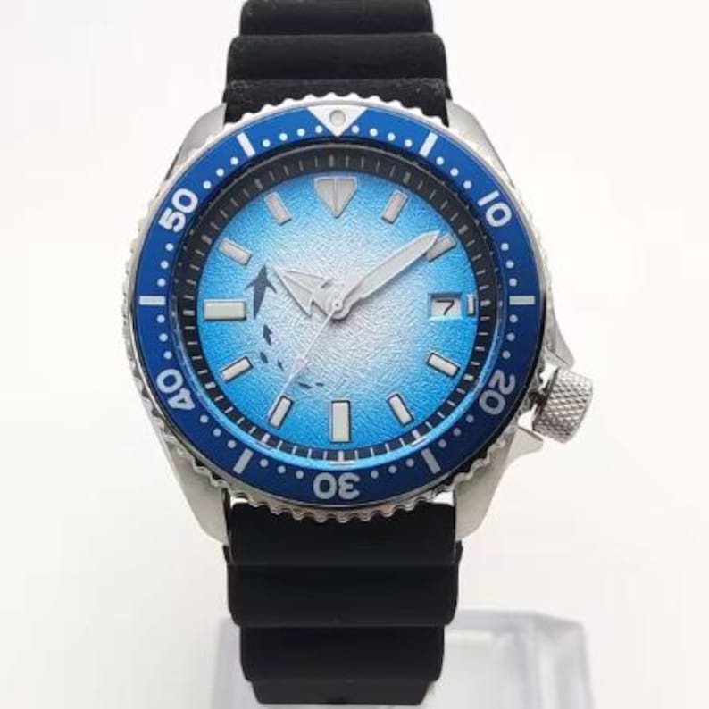 May include: A blue and silver wristwatch with a black rubber band. The watch face has a blue and white gradient with a white fish design. The watch has a rotating bezel with numbers.