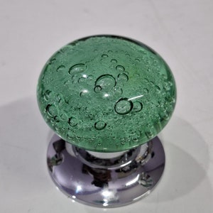 May include: A green glass door knob with a bubbled texture. The knob is attached to a silver base.
