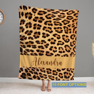 May include: A brown and tan leopard print fleece blanket with a gold bar across the bottom that says "Alexandra" in a cursive font.