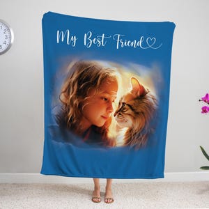 K&ouml;nnte beinhalten: Eine blaue Decke mit einem Portr&auml;t eines M&auml;dchens und einer Katze, mit dem Text "My Best Friend" in wei&szlig;er Schrift. Das M&auml;dchen und die Katze sind in einem weichen, k&uuml;nstlerischen Stil gehalten. Eine Uhr und eine Topf-Orchidee sind im Hintergrund.