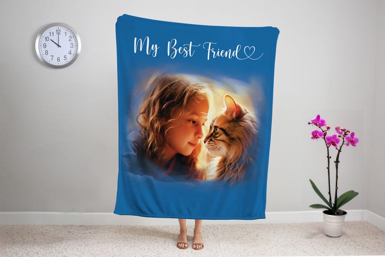 K&ouml;nnte beinhalten: Eine blaue Decke mit einem Portr&auml;t eines M&auml;dchens und einer Katze, mit dem Text "My Best Friend" in wei&szlig;er Schrift. Das M&auml;dchen und die Katze sind in einem weichen, k&uuml;nstlerischen Stil gehalten. Eine Uhr und eine Topf-Orchidee sind im Hintergrund.