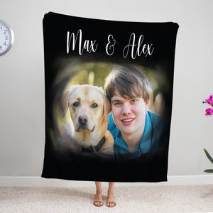 K&ouml;nnte beinhalten: Schwarze Decke mit einem Foto einer Person und einem gelben Labrador Retriever, mit dem Text "Max & Alex" in wei&szlig;er Schrift. Die Decke wird in Innenr&auml;umen mit einer Uhr und einer Topf-Orchidee im Hintergrund pr&auml;sentiert.