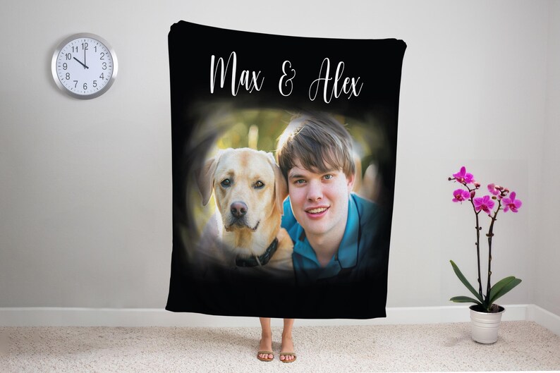 K&ouml;nnte beinhalten: Schwarze Decke mit einem Foto einer Person und einem gelben Labrador Retriever, mit dem Text "Max & Alex" in wei&szlig;er Schrift. Die Decke wird in Innenr&auml;umen mit einer Uhr und einer Topf-Orchidee im Hintergrund pr&auml;sentiert.