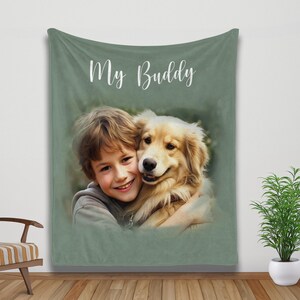 K&ouml;nnte beinhalten: Eine salbeigr&uuml;ne Decke mit den Worten "My Buddy" in wei&szlig;er Schrift. Die Decke zeigt ein Portr&auml;t eines Kindes, das einen Golden Retriever-Hund umarmt. Das Bild hat einen weichen, malerischen Effekt.