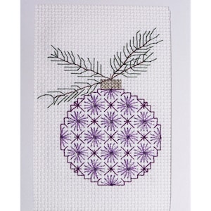 May include: A purple and white cross-stitch ornament with a green sprig on top. The ornament is in a white frame and the text "Sugar Plum Ornament #2" is below the frame.