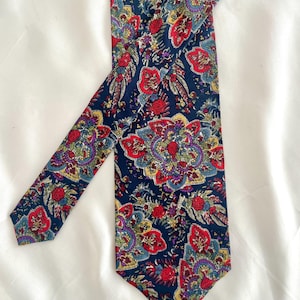 May include: A dark blue silk tie with a paisley pattern in shades of red, green, yellow, and purple.