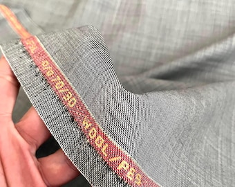 May include: Close-up of gray fabric with a woven texture. A red and gold label with the text "WOOL/PES" and "DE/70/30" is visible along the edge of the fabric. The fabric is held in a hand.