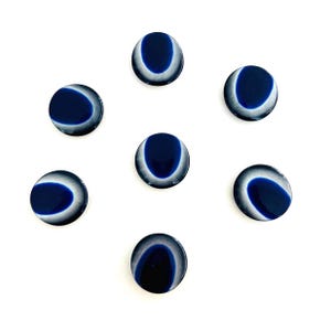 May include: A set of six circular buttons, each featuring a deep navy blue center surrounded by a translucent, iridescent white border. The buttons have a smooth, polished finish and a distinct eye-like pattern created by the contrast between the dark blue core and the lighter outer ring.