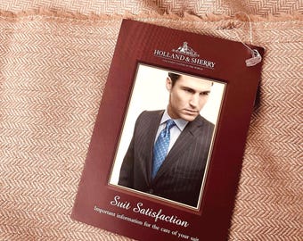 May include: A rectangular burgundy card with the text Holland & Sherry and Suit Satisfaction, Important information for the care of your suit, featuring a photograph of a person in a pinstripe suit and blue tie, resting on a light brown herringbone fabric.