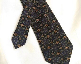 May include: A necktie featuring a dark green and purple geometric pattern with repeating gold floral motifs. The design consists of interlocking angular shapes and circular elements arranged in a structured grid across the fabric surface.