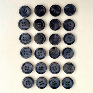 May include: A collection of twenty-one dark gray, round buttons with four holes each. The buttons have a subtle iridescent sheen, and are arranged in a grid pattern against a light background. These buttons are suitable for sewing and craft projects.
