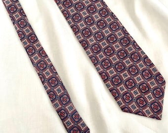 May include: A patterned necktie with a repeating geometric design in shades of burgundy, navy blue, and cream. The tie is displayed on a white surface, showcasing its intricate pattern and color palette. The tie is a classic accessory.