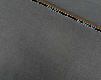May include: Close-up of a gray fabric swatch with a brown label that reads "Made in England" and "Super 100's" with a blue label that reads "Ben  Crispin Paris".