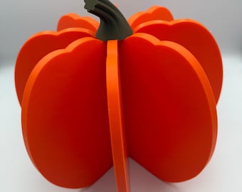 May include: A vibrant orange, three-dimensional pumpkin decoration with a dark green stem. The pumpkin is made from several curved, vertical panels, creating a layered effect. Suitable for autumn and Halloween.