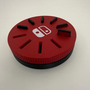 May include: Red and black circular game cartridge storage case with a Nintendo Switch logo. The case has 12 slots for game cartridges.
