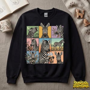 May include: Black sweatshirt featuring a grid of nine zebra illustrations in various poses and settings. Each zebra is depicted in a unique square with colorful backgrounds. The sweatshirt has a crew neck and long sleeves.
