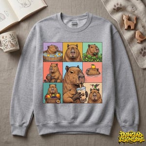 May include: A heather gray sweatshirt featuring a colorful grid of capybara illustrations. Each square depicts a capybara in various activities, such as enjoying a bath, eating, and drinking. The sweatshirt has a crew neck and long sleeves.