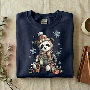 May include: Navy blue sweatshirt featuring a panda bear wearing a plaid hat and scarf, surrounded by snowflakes. The panda is holding candy canes and sitting next to wrapped gifts. The sweatshirt has a crew neck and a tag that says "Gildan".