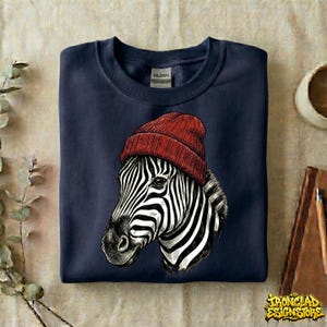 May include: Navy blue sweatshirt featuring a detailed illustration of a zebra wearing a red beanie. The zebra's black and white stripes contrast with the solid navy background. The sweatshirt has a crew neck and a tag that says "Gildan".