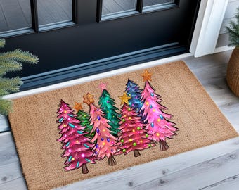 May include: A rectangular doormat featuring a colorful Christmas tree design. The trees are in shades of pink, green, and blue, adorned with star toppers and string lights. The mat is made of a natural fiber material.