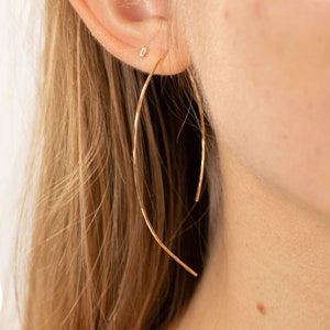 May include: A pair of gold filled hoop earrings, 3 inches (76.20 mm) in diameter. The earrings are thin and delicate, with a slightly curved shape.