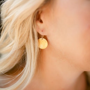 May include: Gold hammered disc earrings with a delicate wire hook. The earrings are a simple and elegant design.
