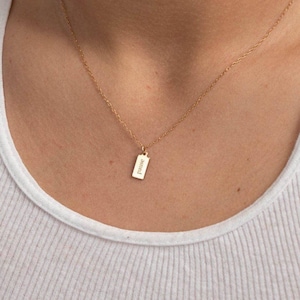 May include: A gold-toned necklace featuring a delicate chain and a small, rectangular pendant. The pendant is engraved with the word "pause" in a simple, lowercase serif font. The necklace rests against the collarbone area.