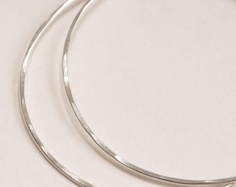 May include: A pair of thin, circular hoop earrings crafted from polished silver-toned metal. The surface of the hoops features a subtle hammered texture, creating small, reflective facets along the rounded wire structure of the jewelry pieces.