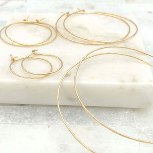 May include: A collection of four gold hoop earrings in varying sizes, featuring a thin, circular wire design with a subtle hammered texture. The set includes two pairs of hoops, each with a simple post closure, arranged in a cluster.