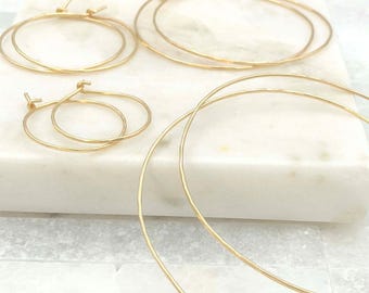 May include: A collection of four gold hoop earrings in varying sizes, featuring a thin, circular wire design with a subtle hammered texture. The set includes two pairs of hoops, each with a simple post closure, arranged in a cluster.
