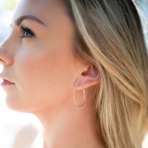 May include: A close-up shot of a person wearing a pair of thin, gold hoop earrings. The earrings are circular and have a simple, elegant design. The person has blonde hair and is looking to the side.