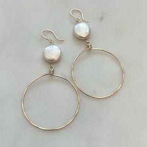 May include: A pair of gold hoop earrings with a single white pearl dangling from each hoop.