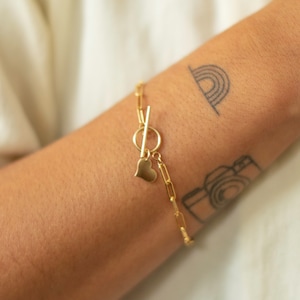 May include: A gold chain bracelet with a heart charm and a toggle clasp.