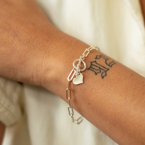 May include: A silver chain bracelet with a heart charm and a toggle clasp.